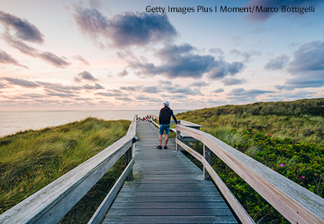 Teaser_mBN_TourismusNordsee Tourist auf einem Weg aus Holzplanken bei Sonnenuntergang auf der Insel Sylt