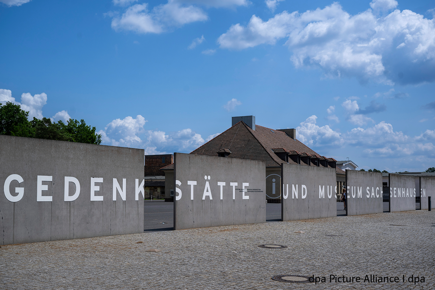 Mit der WebApp „Dingen auf der Spur“ Gedenkstättenbesuche vorbereiten: Bild der Gedenkstätte und des Museum Sachsenhausen. Im Vordergrund ist eine unterbrochene Mauer aus Beton zu sehen, die aus zwei Teilen besteht. Auf den Teilstücken ist in großen weißen Buchstaben das Wort "Gedenkstätte" zu lesen. Hinter der Mauer sind Häuser als Teile der Gedenkstätte zu erkennen.: Im Vordergrund ist eine Mauer aus Beton zu sehen, die aus mehreren Teilen besteht bzw. unterbrochen ist. Die Mauer umschließt das Gelände der Gedenkstätte. Auf den Teilstücken ist in großen weißen Buchstaben der Schriftzug "Gedenkstätte und Museum Sachsenhausen" zu lesen. Hinter der Mauer sind Häuser als Teile der Gedenkstätte zu erkennen.