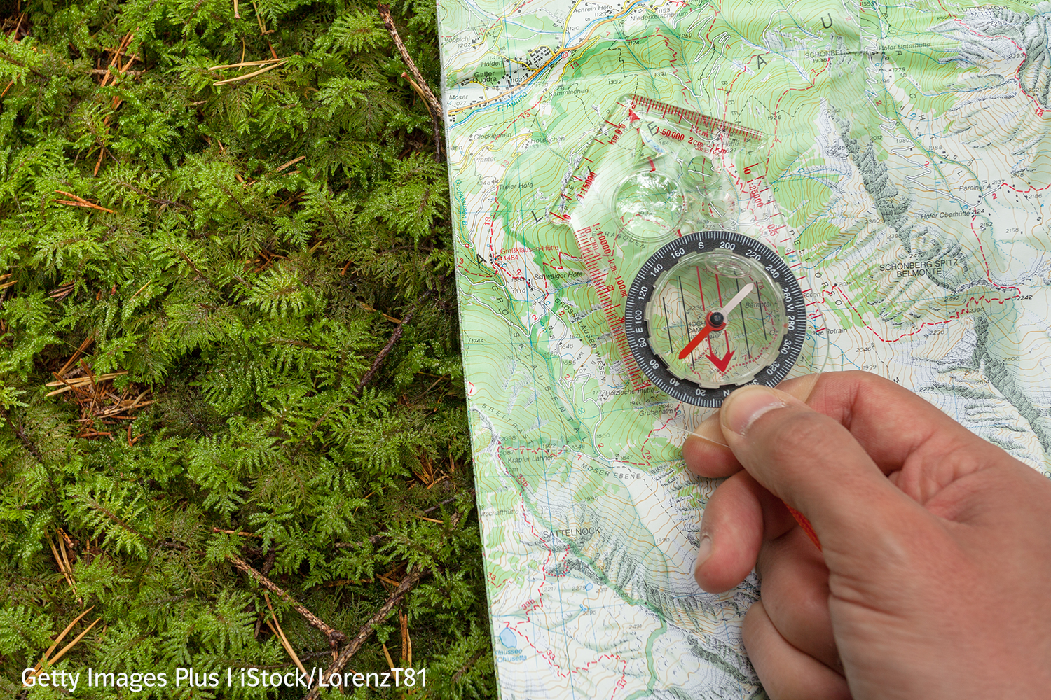 Beitrag_mBN_InterviewMehren1 Eine topographische Karte der Gailtaler Alpen in Österreich liegt auf einem Waldboden mit Moos. Eine Hand hält zur Orientierung einen Kompass mit Maßstabsleiste und Lupe über die Karte.