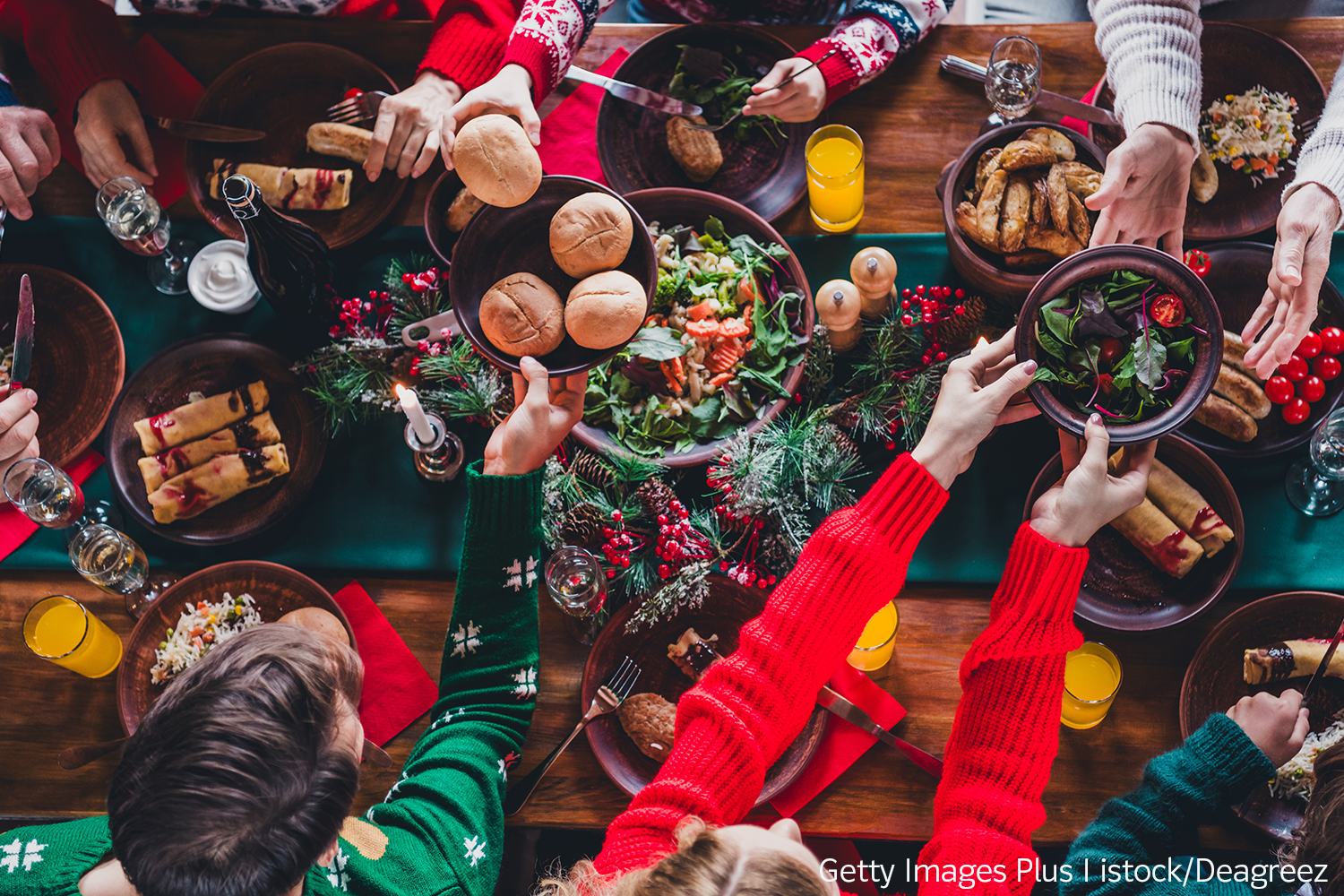 Beitrag_mBN_NachhaltigeWeihnachten3 Blick von oben auf eine weihnachtlich dekorierte Essenstafel, an der mehrere Kinder und Jugendliche in weihnachtlicher Kleidung sitzen. Sie reichen sich gegenseitig die Speisen auf Schüsseln und Tellern an.