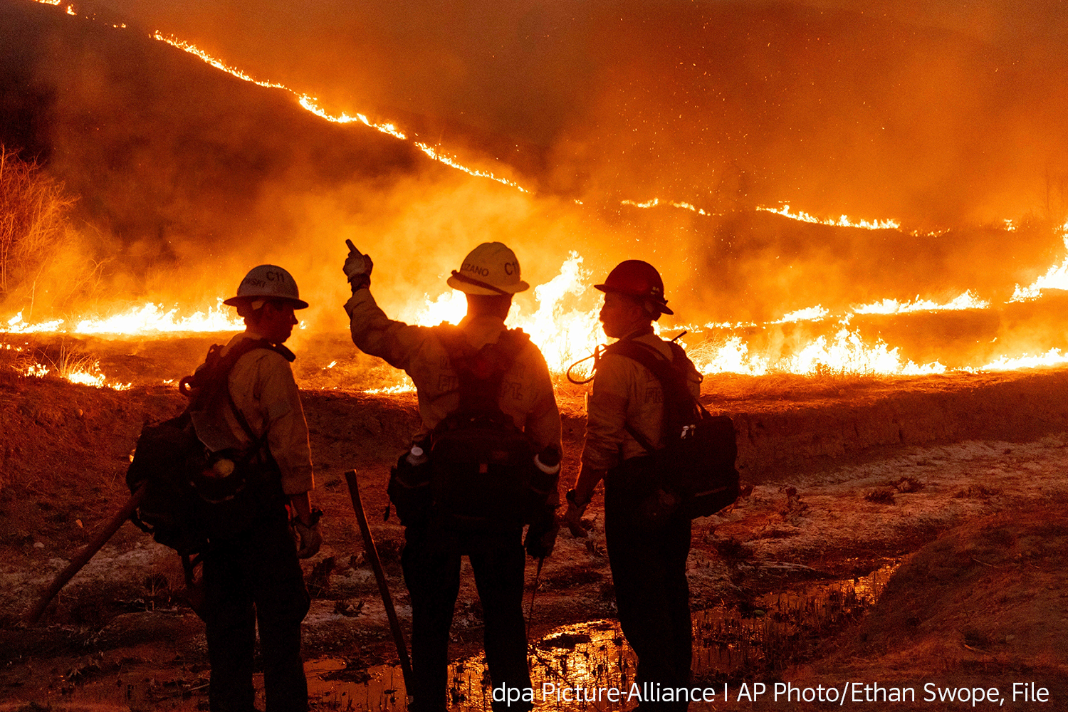drei Feuerwehrmänner stehen in der Nacht vor einem Flächenbrand in Los Angeles und beraten über die nächsten Schritte
