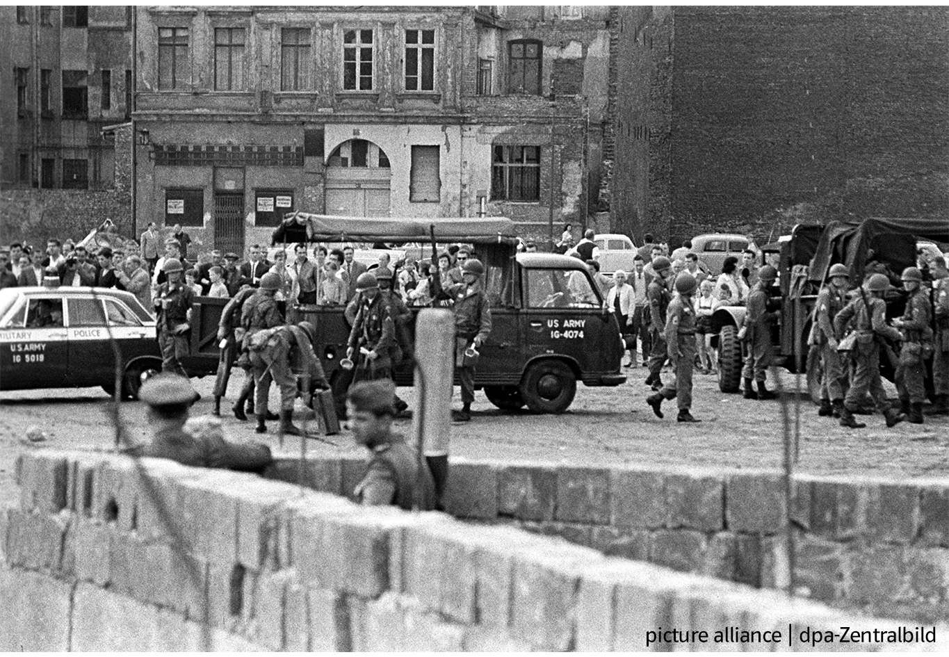 Berliner Mauer: Wenige Tage nach dem 13.08.1961 verstärkt die amerikanische Militärpolizei ihre Präsenz an der Sektorengrenze zu Ostberlin nahe Friedrichstraße - unter Beobachtung der Westberliner Bevölkerung auf der einen Seite, zweier Volkspolizisten der DDR "vor" der neu errichteten Mauer auf der anderen Seite.