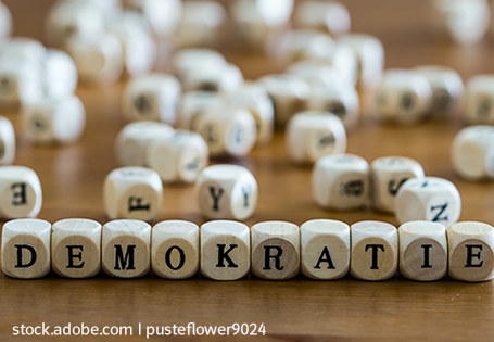 Kleine weiße Holzwürfel auf einem Tisch, bedruckt mit Buchstaben und aneinandergereiht zum Wort DEMOKRATIE
