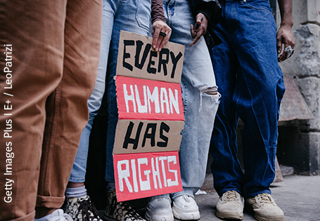 Vier Jugendliche stehen auf einer Straße und halten ein Demonstrationsplakat mir der der Aufschrift "Every Human Has Rights".