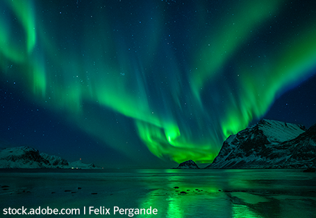Grüne Polarlichter über einem Fjord. Schneebedeckte Berge umschließen den Fjord rechts und links.